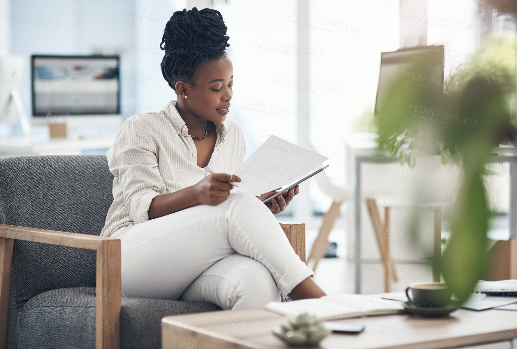 Buy stock photo Shot of a businesswoman using her digital tablet while reading paperwork