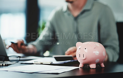 Buy stock photo Shot of an unrecognizable businessman doing paperwork with a piggybank on his desk at work