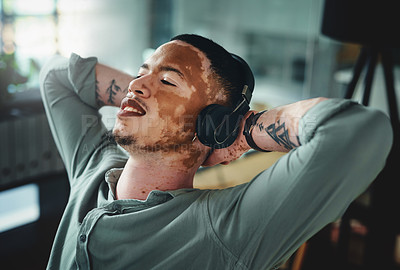 Buy stock photo Shot of a young businessman wearing headphones while taking a nap in an office