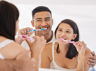 Buy stock photo Shot of a happy young couple standing together in their bathroom and brushing their teeth
