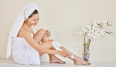 Buy stock photo Full length shot of an attractive young woman sitting alone in her bathroom and shaving her legs after her shower