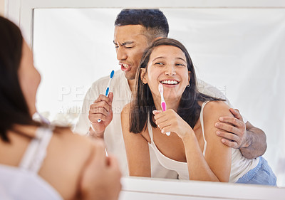 Buy stock photo Shot of a happy young couple standing together in their bathroom and feeling playful while brushing their teeth