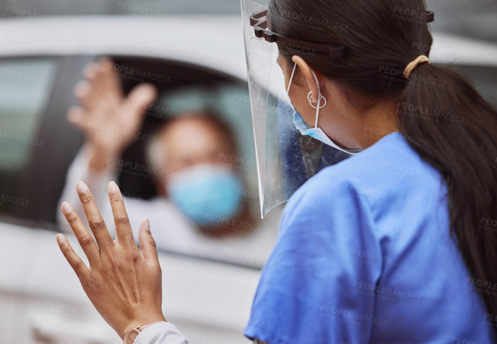 Buy stock photo Shot of an unrecognizable healthcare worker waving at a patient at a drive through vaccination site