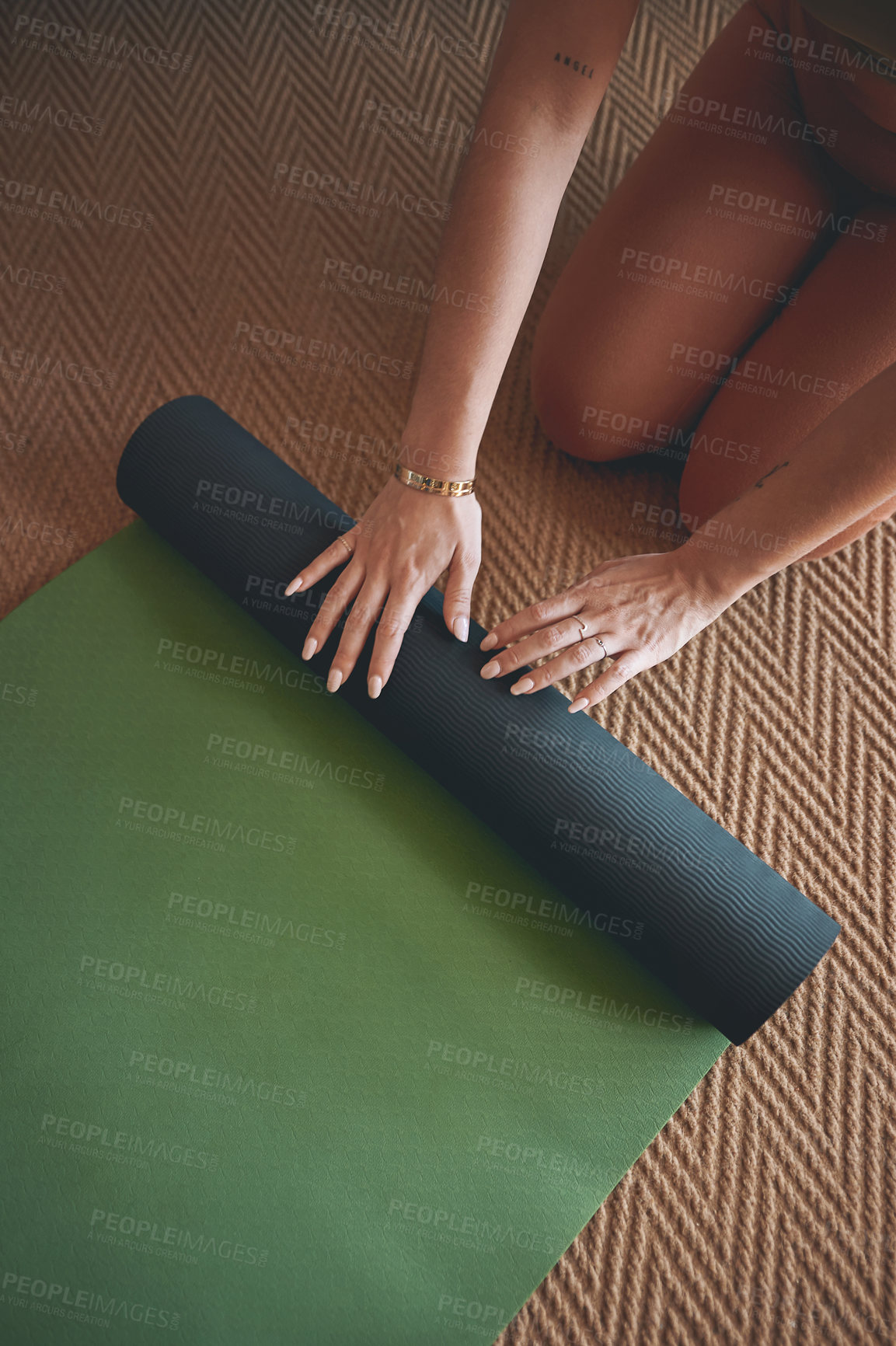 Buy stock photo High angle shot of an unrecognisable woman rolling a yoga mat while exercising at home