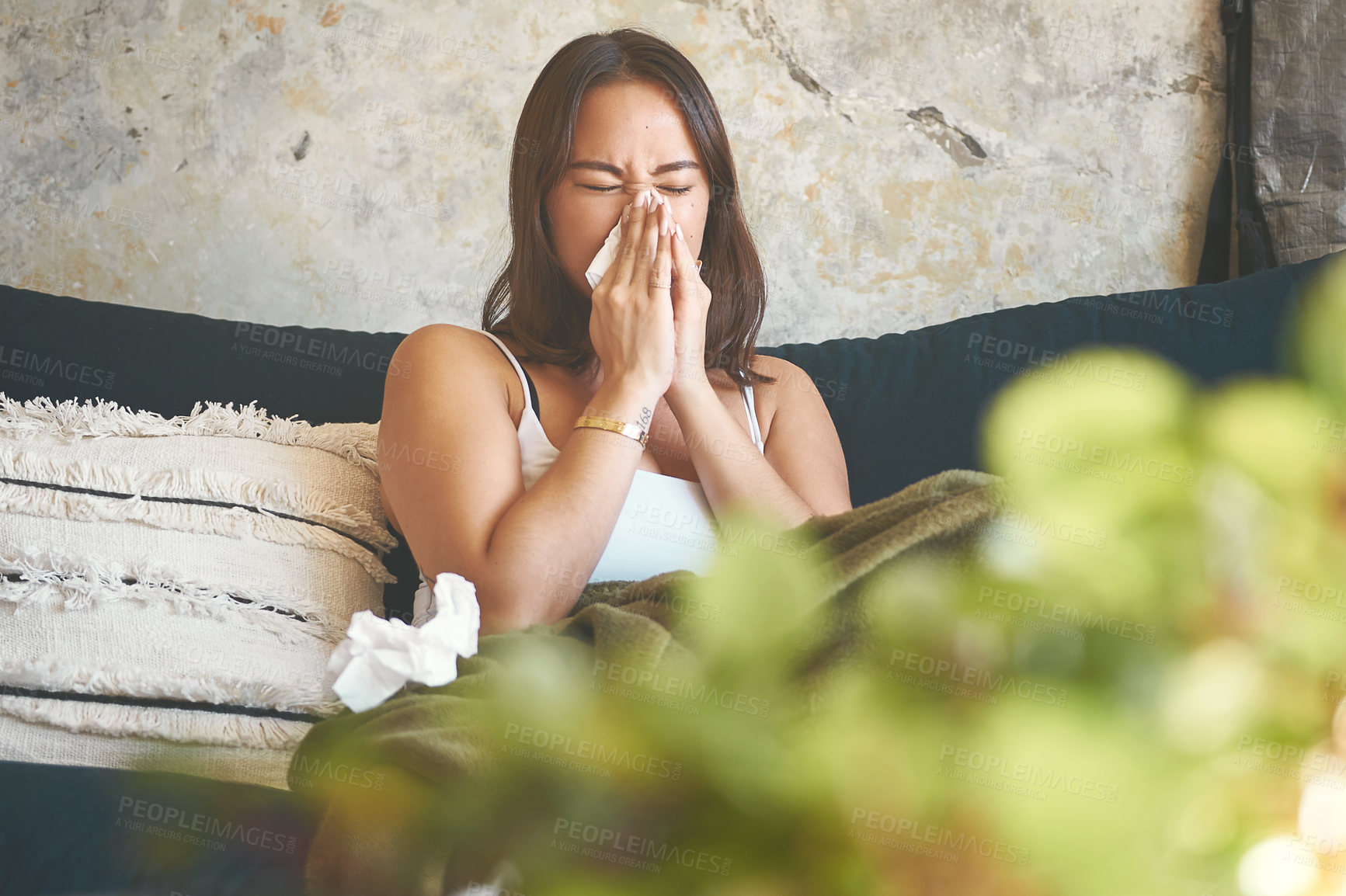 Buy stock photo Shot of a young woman blowing her nose while recovering from an illness on the sofa at home