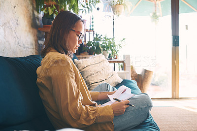 Buy stock photo Shot  of a young woman making notes while relaxing on the sofa at home