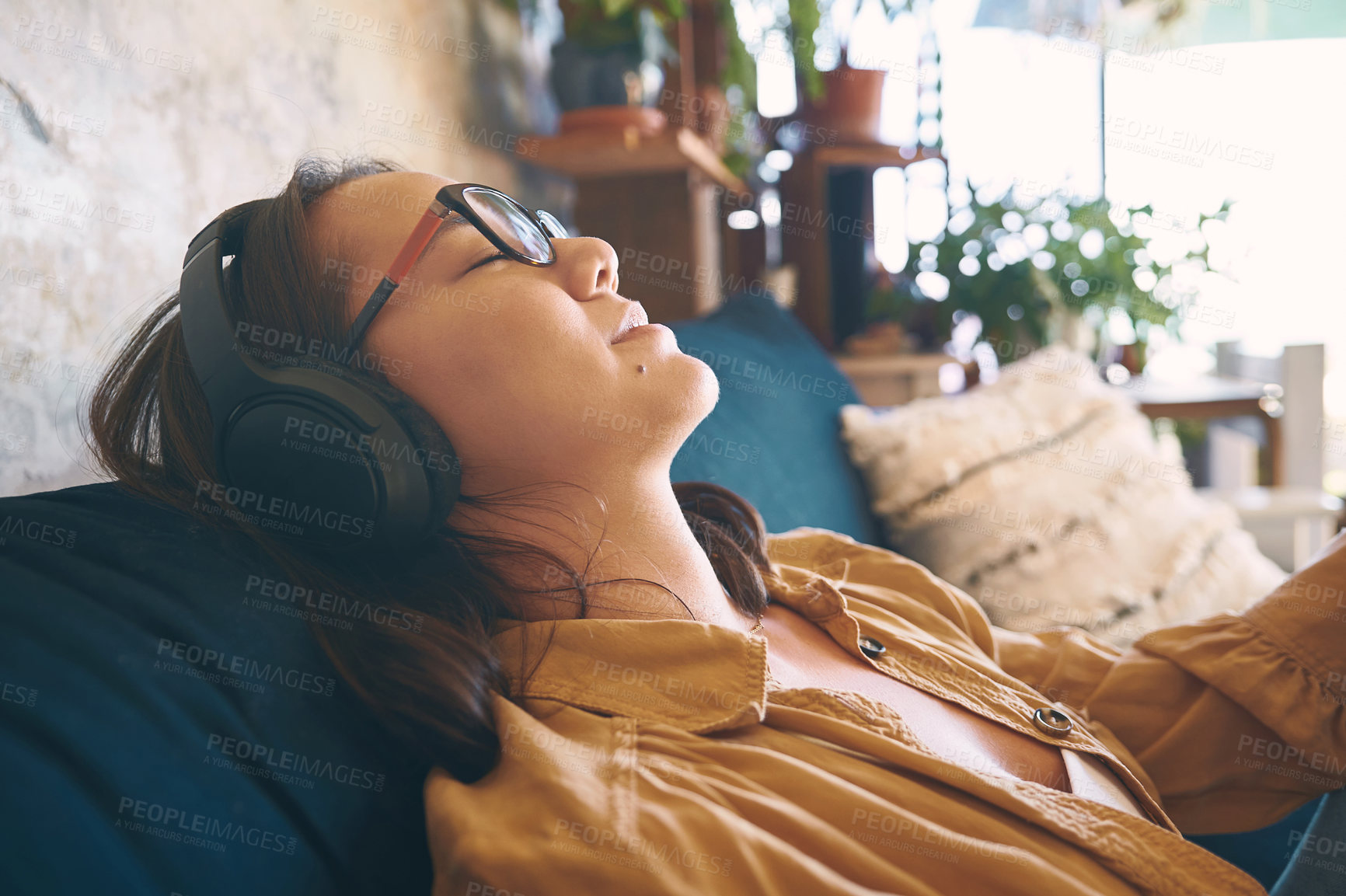 Buy stock photo Shot of a young woman using headphones while relaxing on the sofa at home