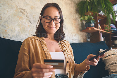 Buy stock photo Shot of a young woman using a smartphone and credit card on the sofa at home