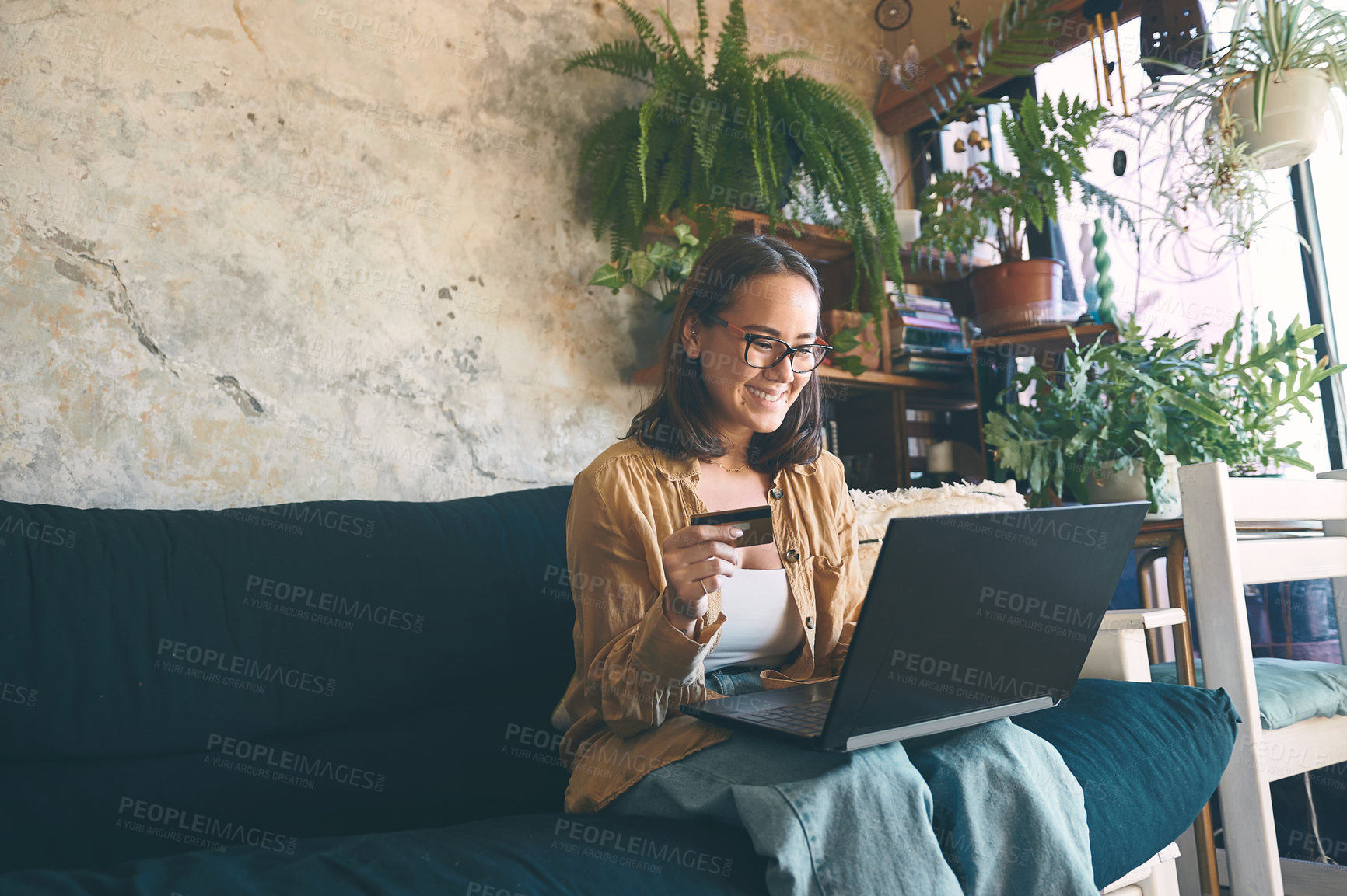 Buy stock photo Shot of a young woman using a laptop and credit card on the sofa at home