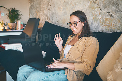 Buy stock photo Shot of a young woman using a laptop to make a video call on the sofa at home