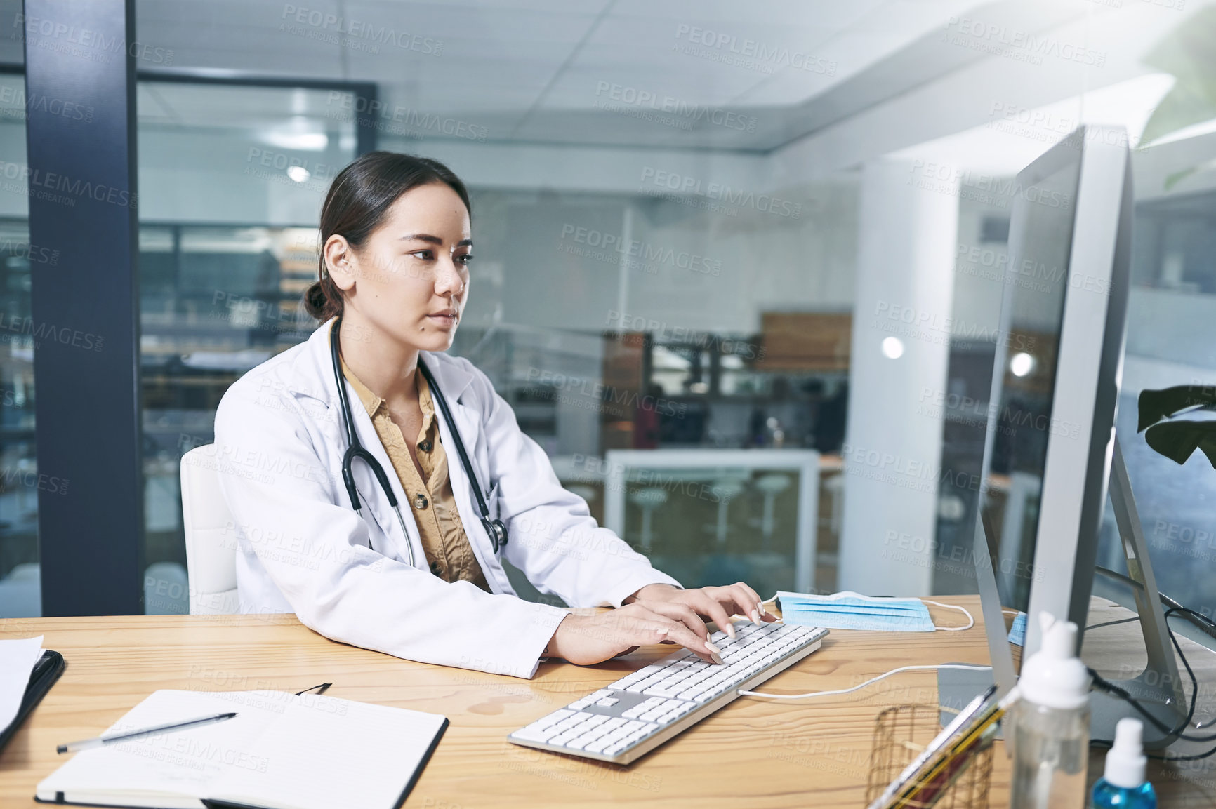 Buy stock photo Shot of an attractive young doctor sitting alone in her office at the clinic and using her computer