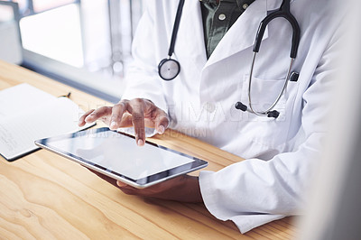 Buy stock photo Cropped shot of an unrecognizable doctor sitting alone in his office at the clinic and using his digital tablet