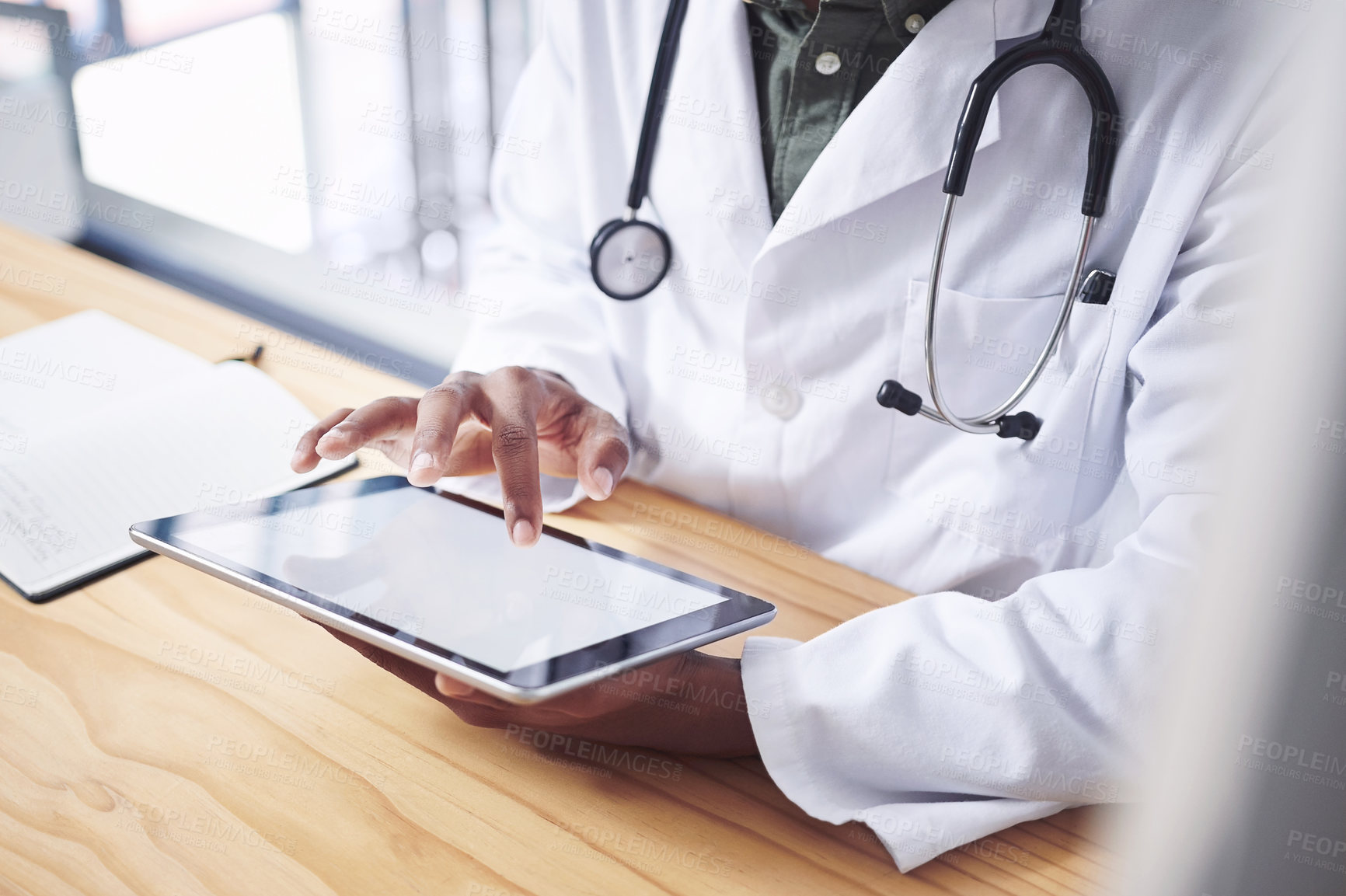 Buy stock photo Cropped shot of an unrecognizable doctor sitting alone in his office at the clinic and using his digital tablet