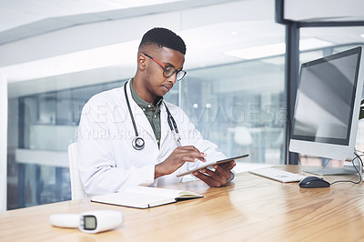 Buy stock photo Shot of a handsome young doctor sitting alone in his office at the clinic and using his digital tablet