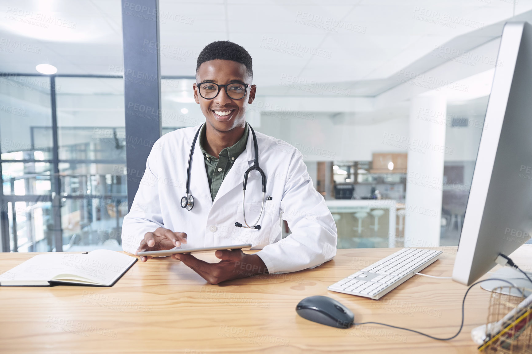 Buy stock photo Shot of a handsome young doctor sitting alone in his office at the clinic and using his digital tablet