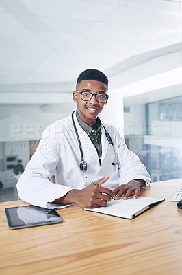 Buy stock photo Shot of a handsome young doctor sitting alone in his office at the clinic and using his notebook