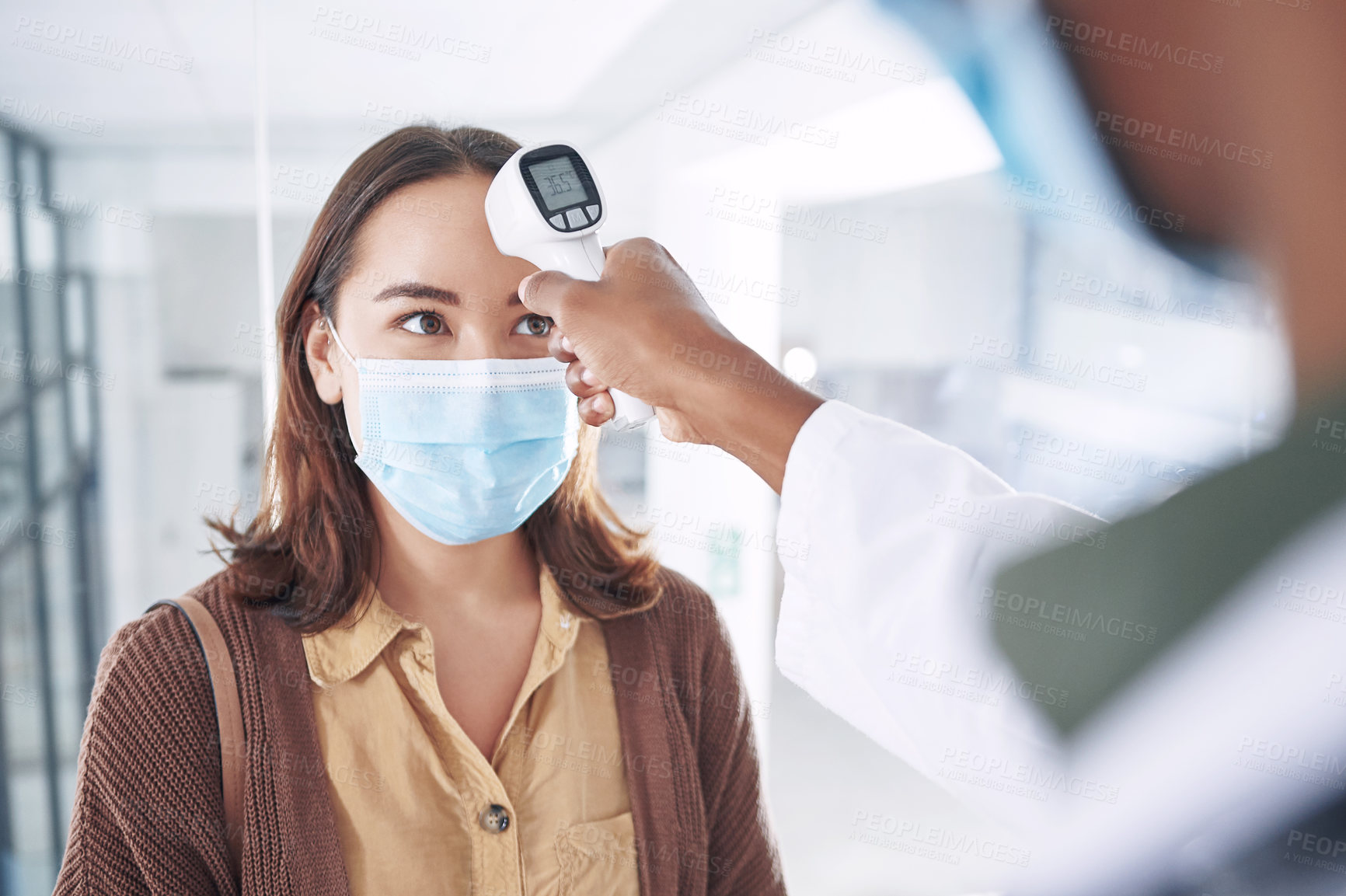 Buy stock photo Shot of a young woman wearing a mask and getting her temperature checked by her doctor in the clinic