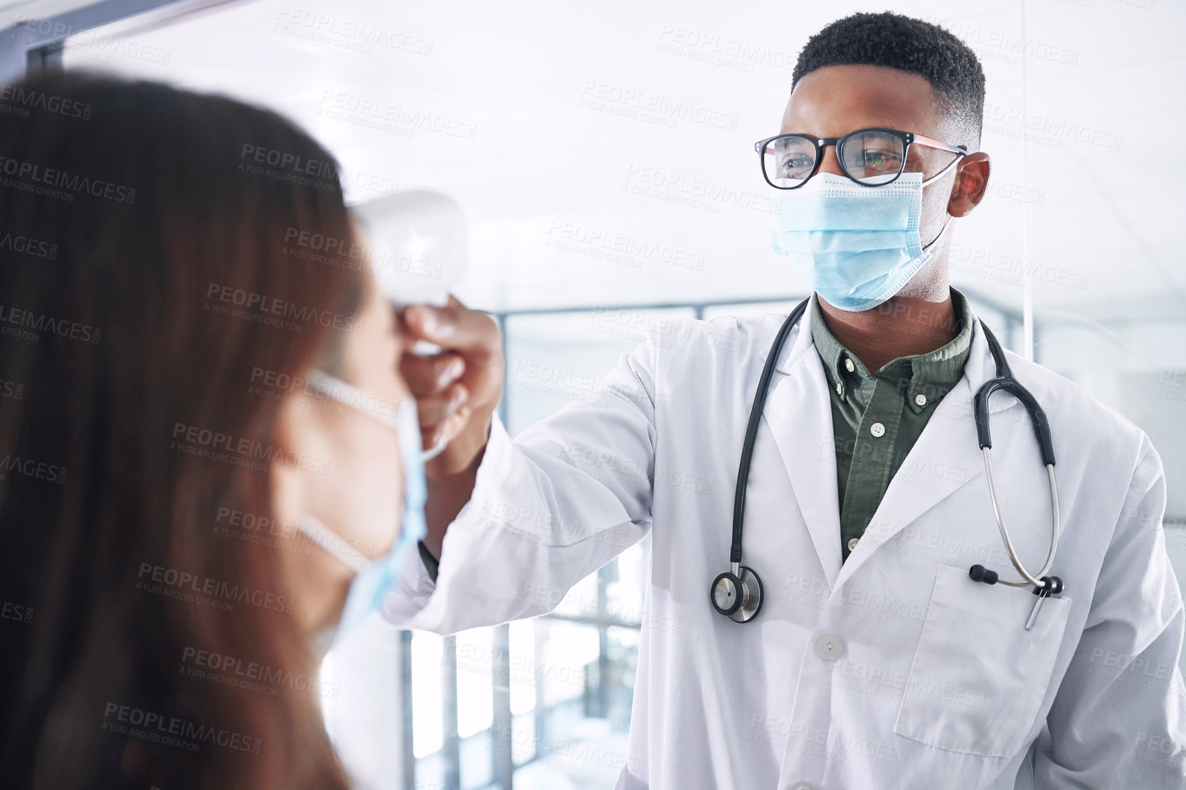 Buy stock photo Shot of a young doctor wearing a mask and standing with a patient in the clinic while taking her temperature