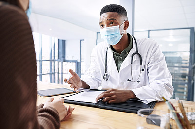 Buy stock photo Shot of a young doctor sitting with his patient and wearing his face mask during a consultation in the clinic