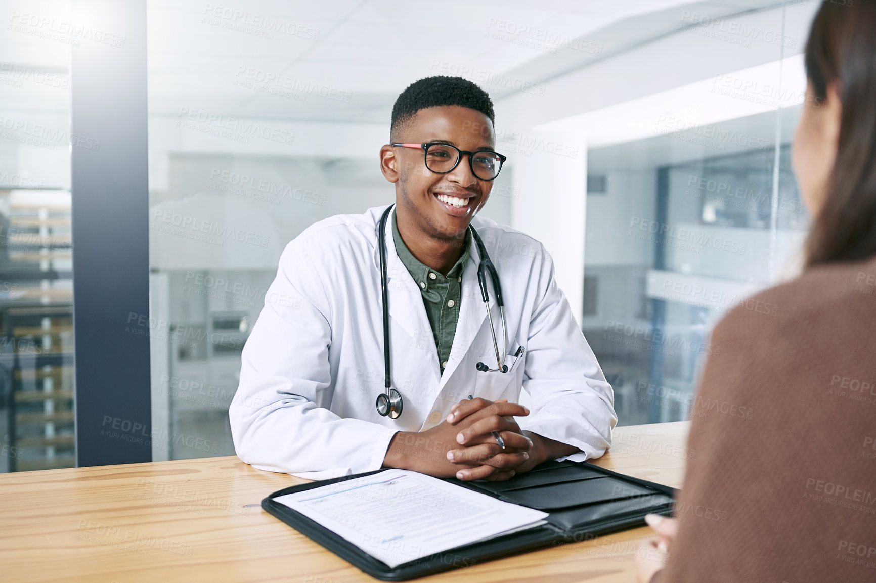 Buy stock photo Shot of a handsome young doctor sitting with his patient during a consultation in the clinic