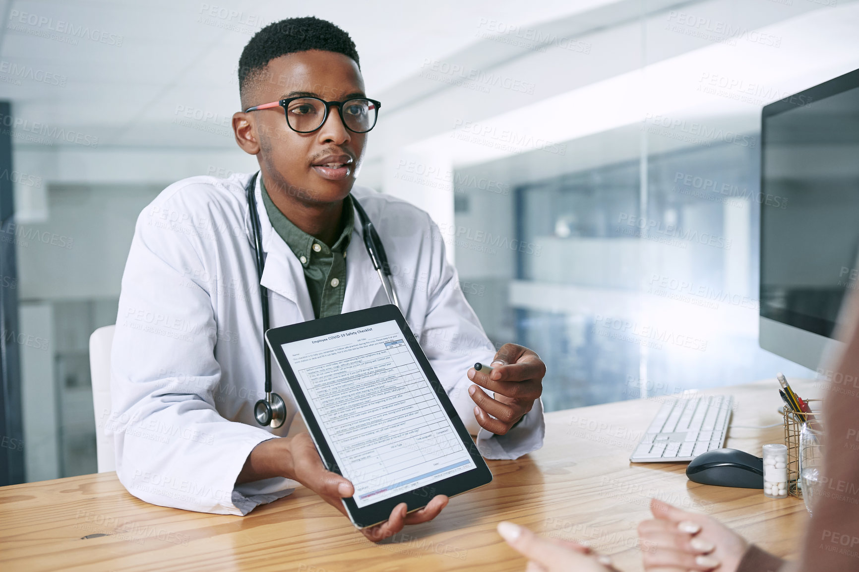 Buy stock photo Shot of a young doctor sitting with his patient and using a digital tablet during a consultation in the clinic