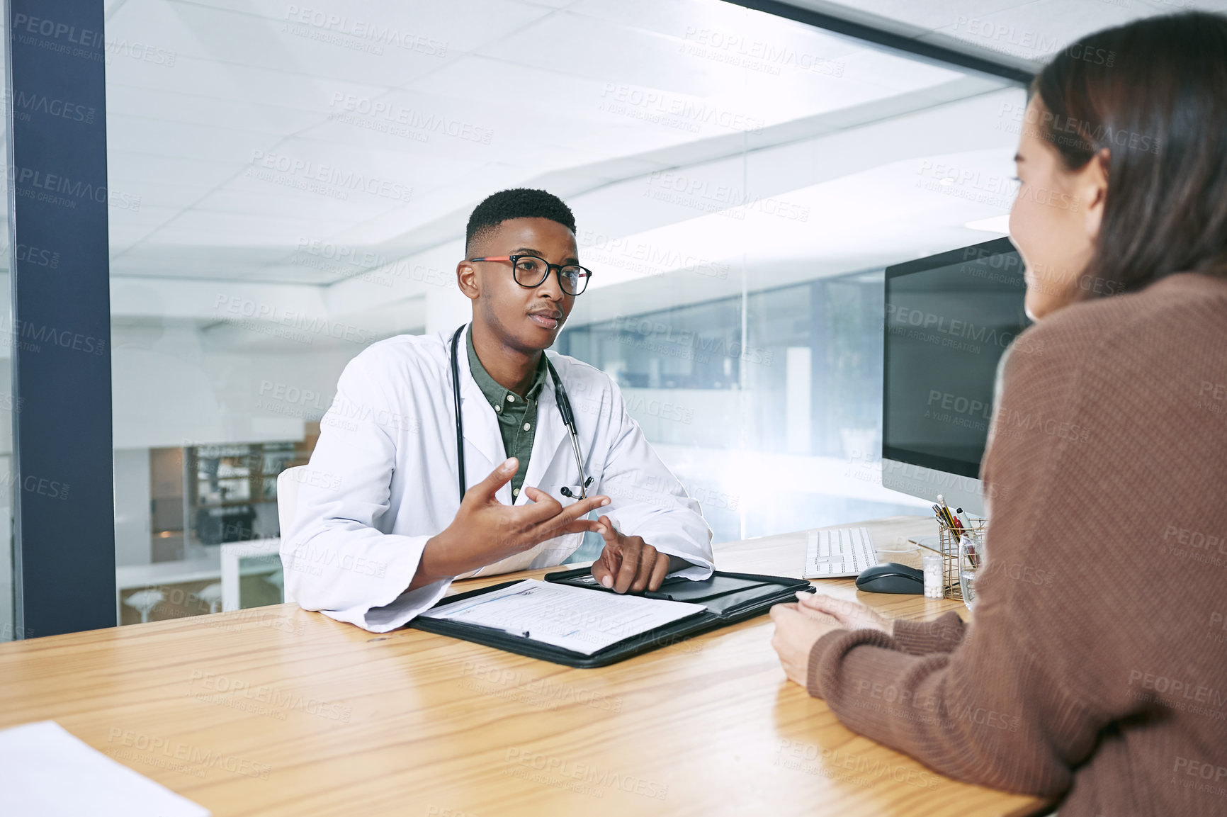 Buy stock photo Shot of a handsome doctor sitting with his patient and explaining her diagnosis during a consultation in the clinic