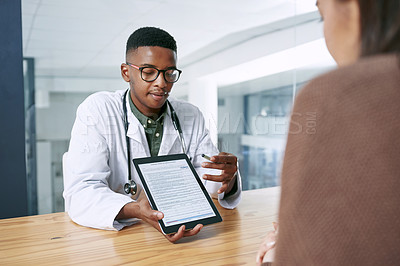Buy stock photo Shot of a young doctor sitting with his patient and using a digital tablet during a consultation in the clinic