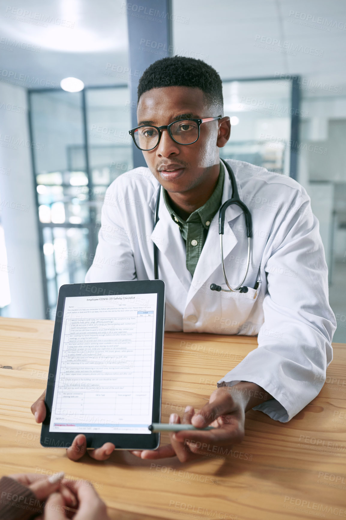 Buy stock photo Shot of a young doctor sitting with his patient and using a digital tablet during a consultation in the clinic