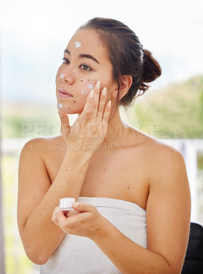 Buy stock photo Shot of a young woman applying moisturiser to her face during her morning beauty routine