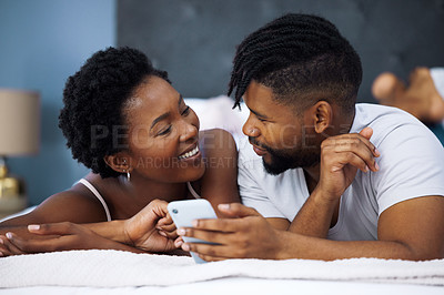 Buy stock photo Shot of a young couple using a smartphone in bed at home