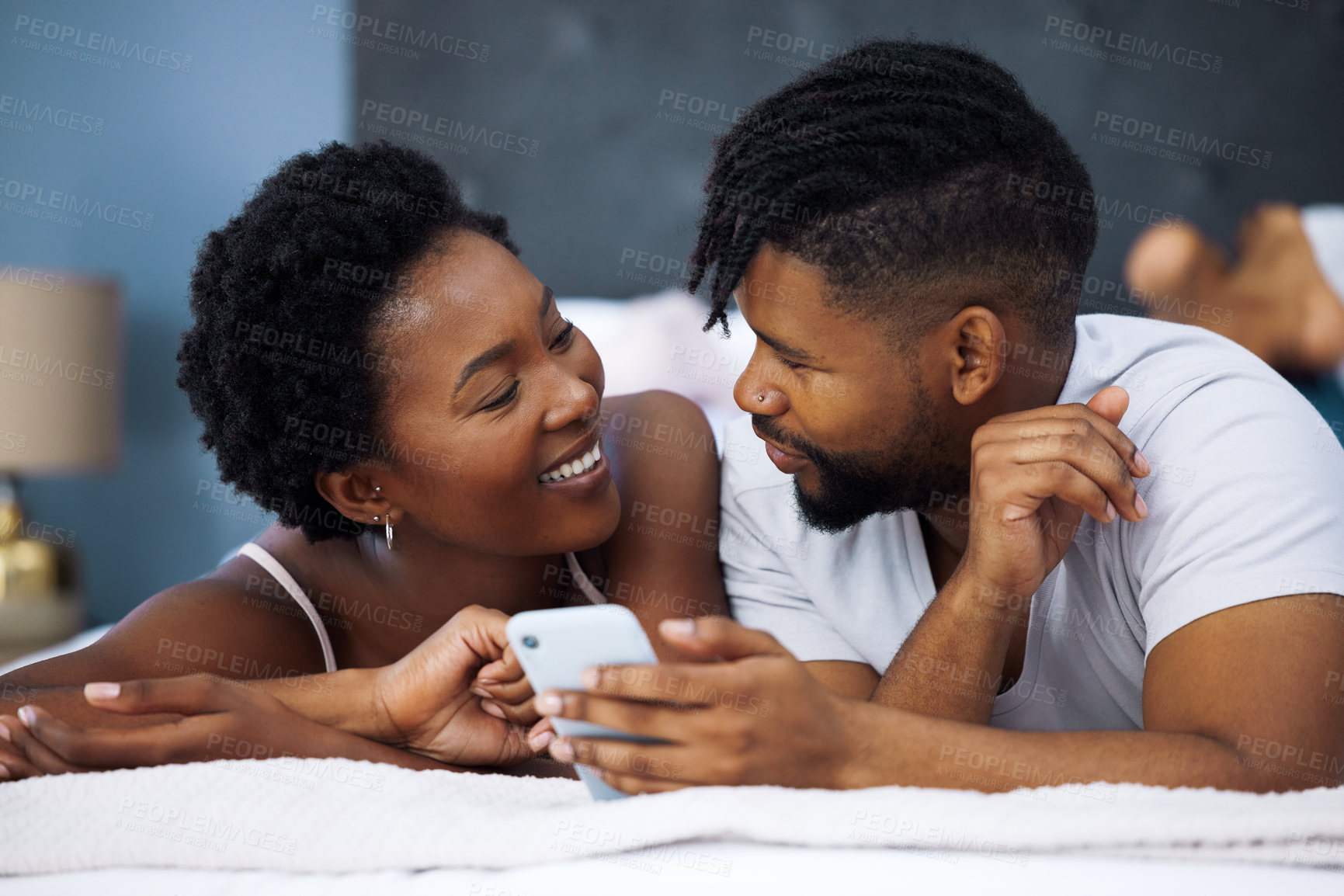 Buy stock photo Morning, mobile and black couple lying on bed for social media, connection or relax in bedroom. Online, romantic man and happy woman with love for text, browsing internet or weekend rest in home