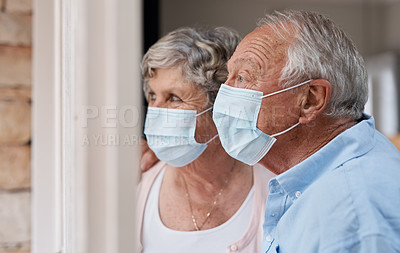 Buy stock photo Shot of a masked elderly couple looking through the window at home