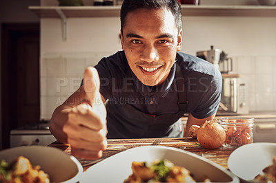 Buy stock photo Portrait of a young man showing thumbs up while preparing a delicious meal at home