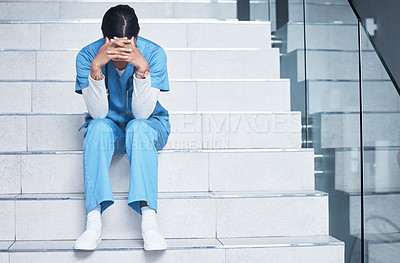 Buy stock photo Shot of a female nurse looking stressed while sitting on a staircase