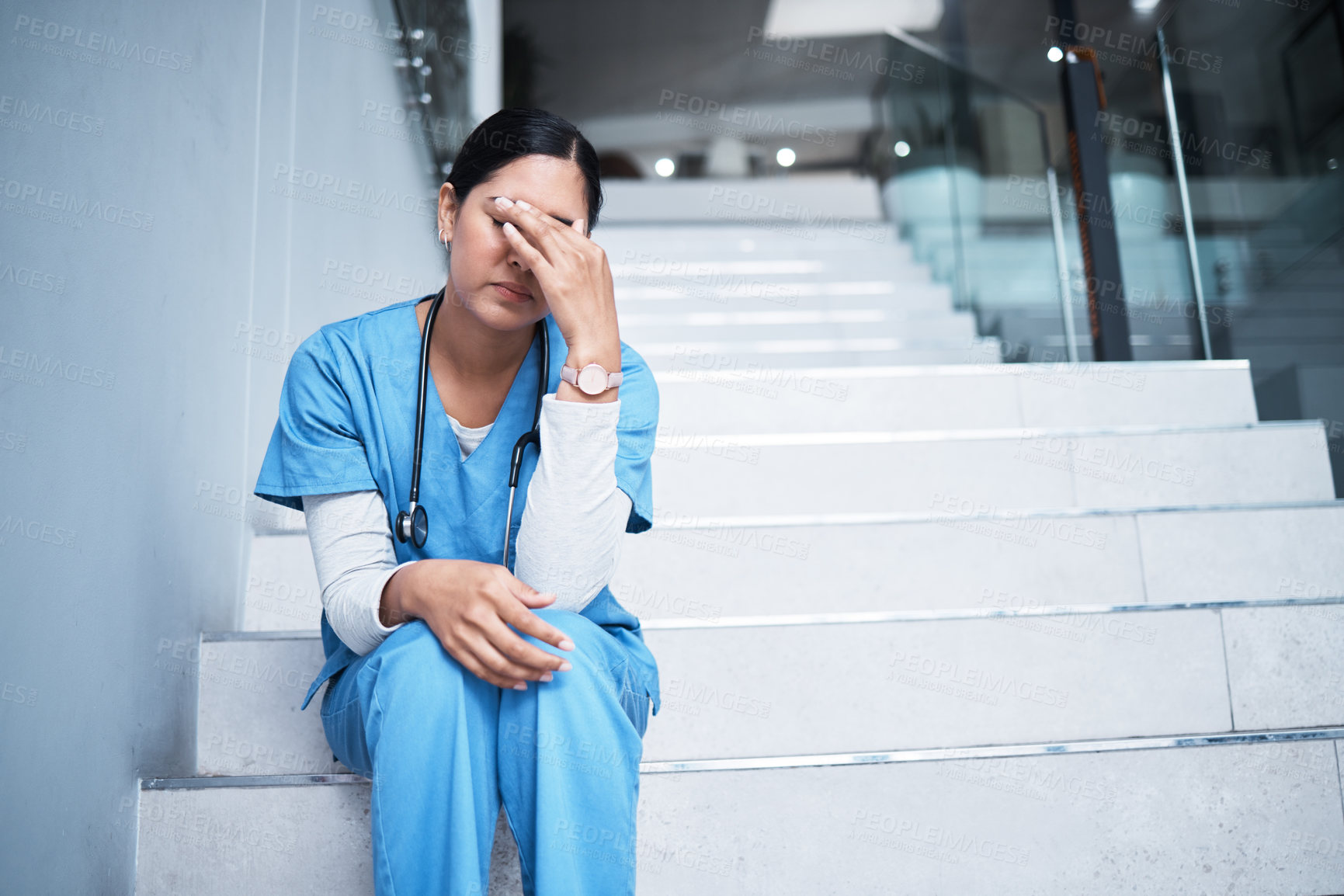 Buy stock photo Shot of a female nurse looking stressed while sitting on a staircase