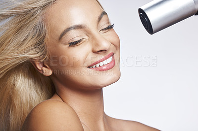 Buy stock photo Shot of an attractive young woman standing alone against a grey background in the studio and using a hairdryer