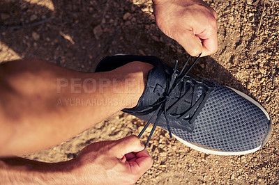 Buy stock photo High angle shot of an unrecognisable man tying his shoelaces while exercising outdoors