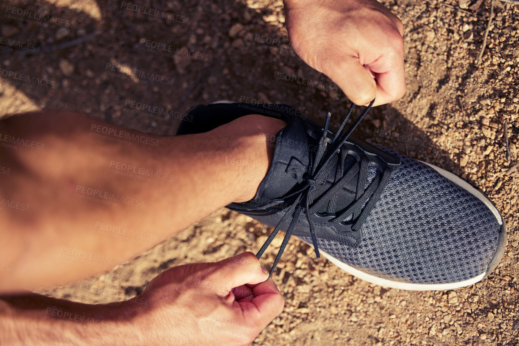 Buy stock photo High angle shot of an unrecognisable man tying his shoelaces while exercising outdoors