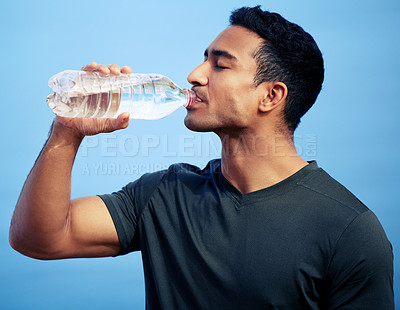 Buy stock photo Fitness, drinking water and man with bottle in studio isolated on a blue background. Liquid, health and male athlete drink after exercise, workout or training for wellness, nutrition and hydration.