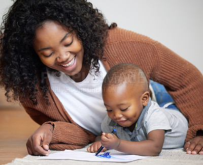 Buy stock photo Shot of an attractive young mother lying on the living room floor with her son and watching him draw