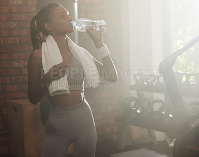 Buy stock photo Shot of a sporty young woman drinking water in a gym