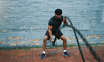 Buy stock photo Shot an athletic young man doing battle rope waves