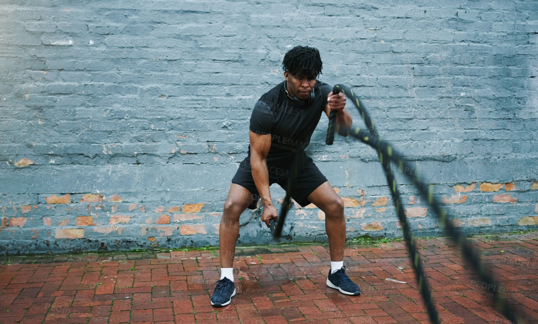 Buy stock photo Shot an athletic young man doing battle rope waves