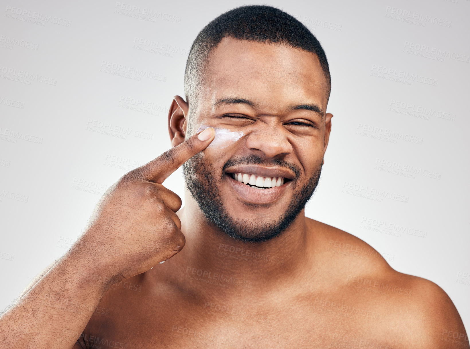 Buy stock photo Studio portrait of a handsome young man applying moisturiser to his face against a white background