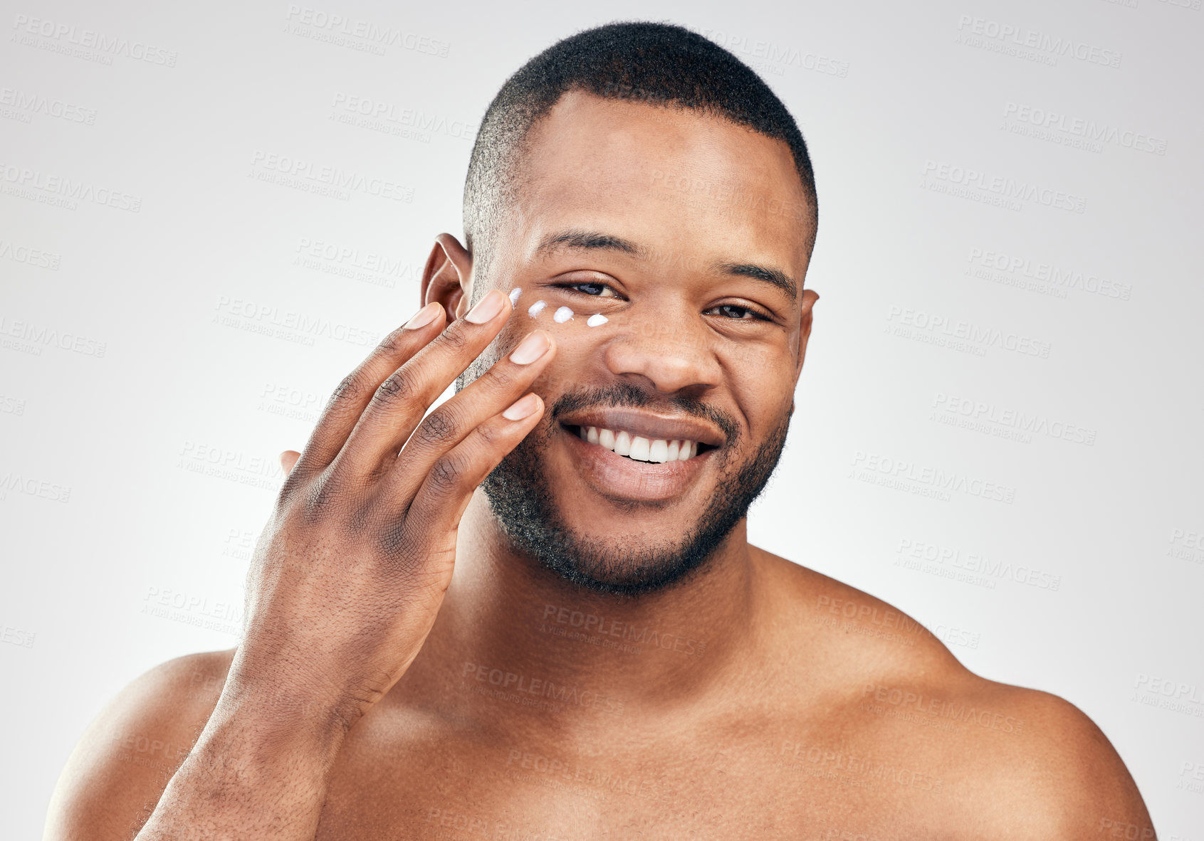 Buy stock photo Studio portrait of a handsome young man applying moisturiser to his face against a white background