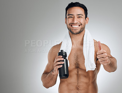 Buy stock photo Shot of an athletic young man showing thumbs up while standing against a grey background with a bottle of water
