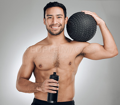 Buy stock photo Shot of an athletic young man posing against a grey background while holding a water bottle and a medicine ball