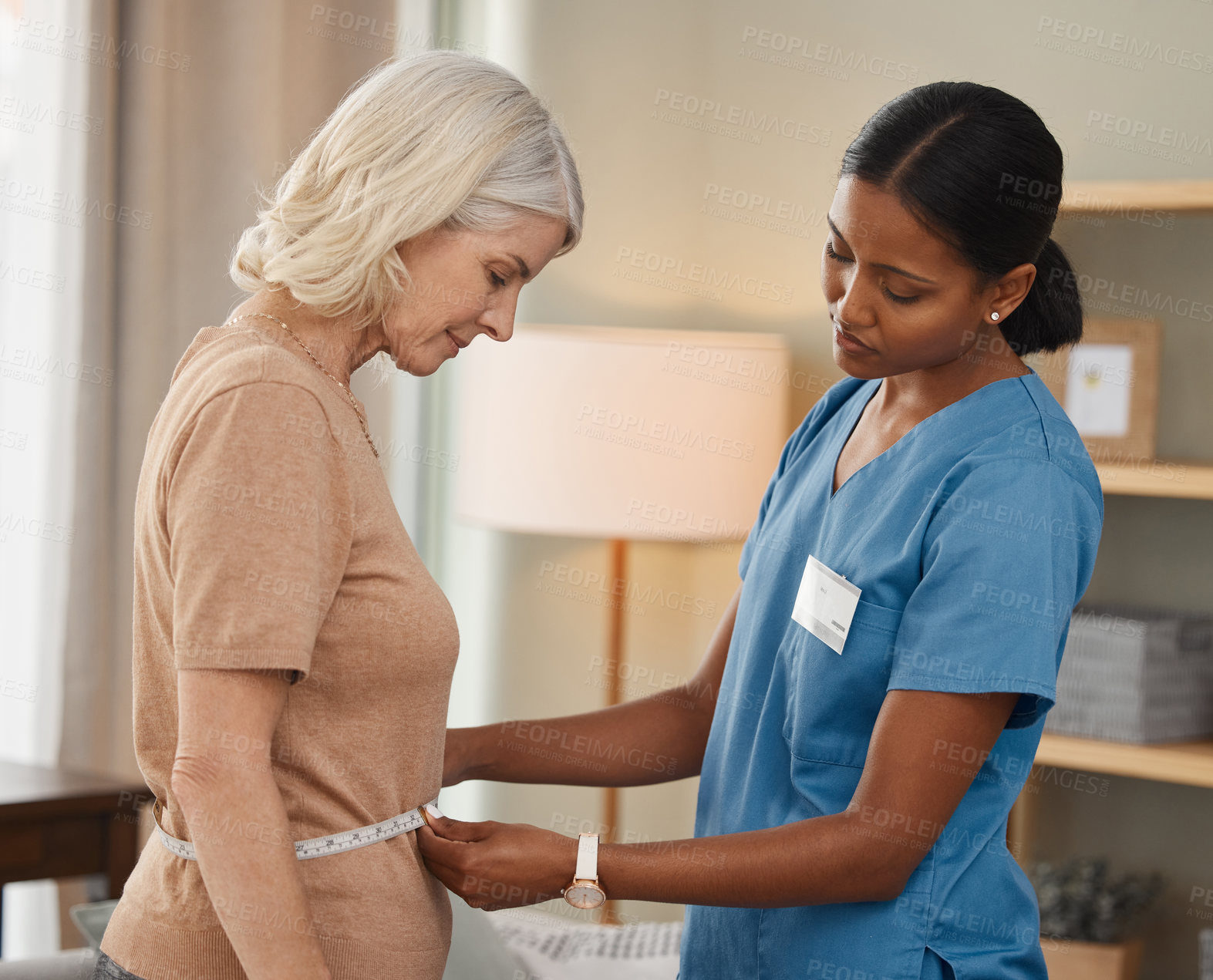 Buy stock photo Shot of a doctor using a measuring tape on a senior woman’s stomach during a consultation at home