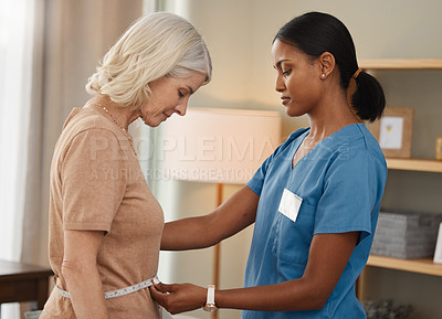 Buy stock photo Shot of a doctor using a measuring tape on a senior woman’s stomach during a consultation at home
