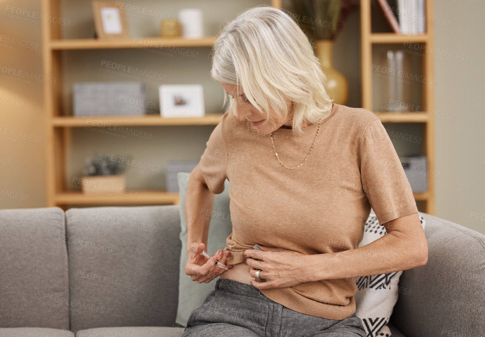 Buy stock photo Shot of a mature woman injecting herself with insulin on the sofa at home